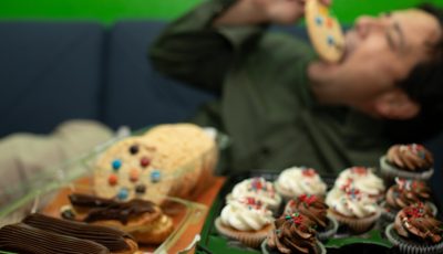 Man laying down eating cookies and cupcakes.